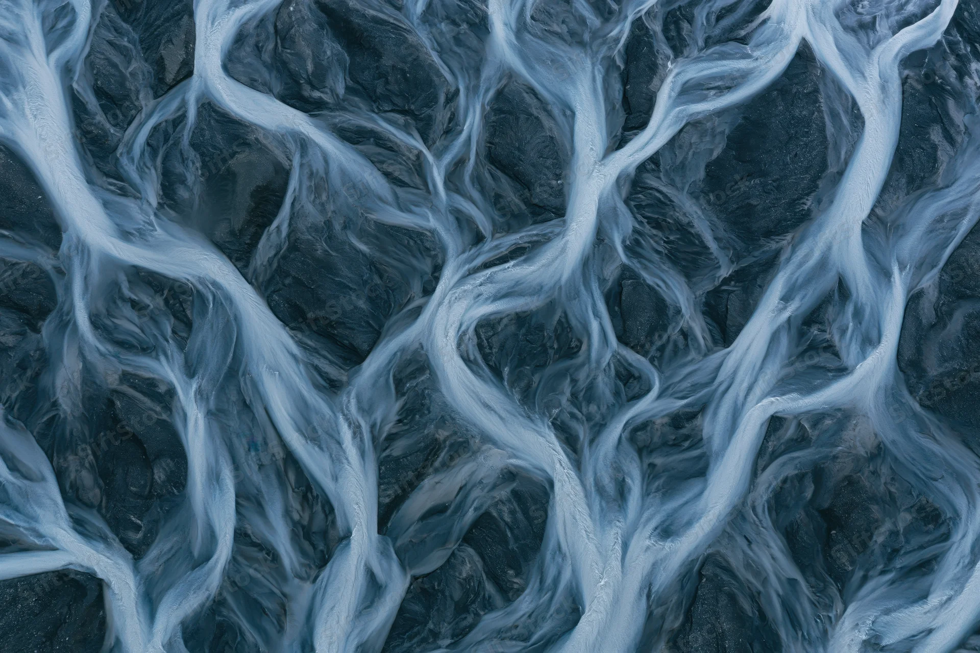 Aerial topdown view of a braided glacial river delta with branching water channels flowing over dark terrain