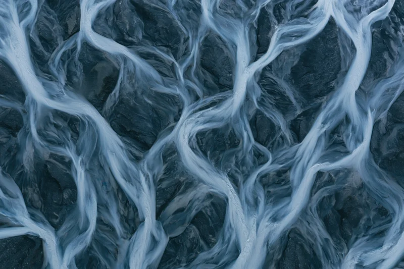 Aerial topdown view of a braided glacial river delta with branching water channels flowing over dark terrain