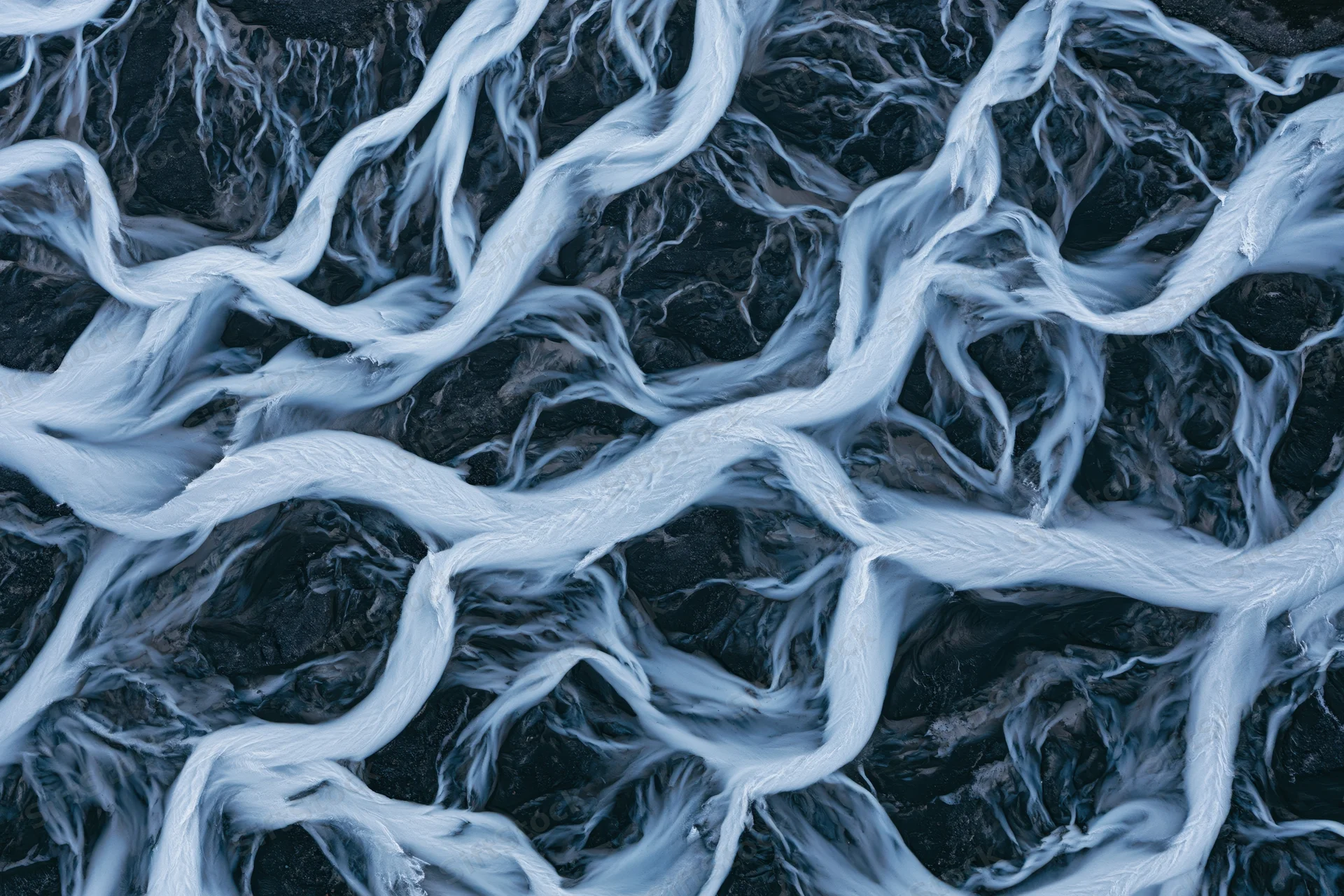 Braided glacial river flowing over dark rocky terrain from above