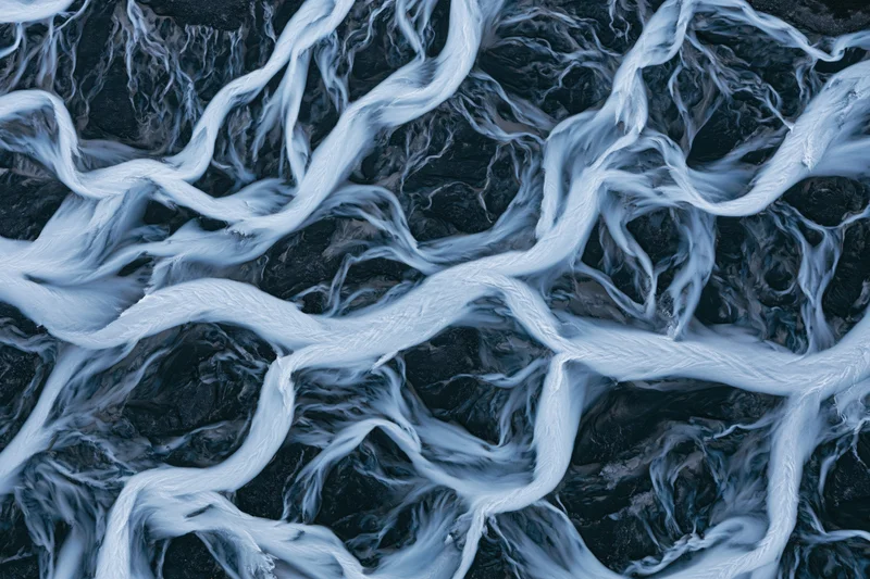 Braided glacial river flowing over dark rocky terrain from above