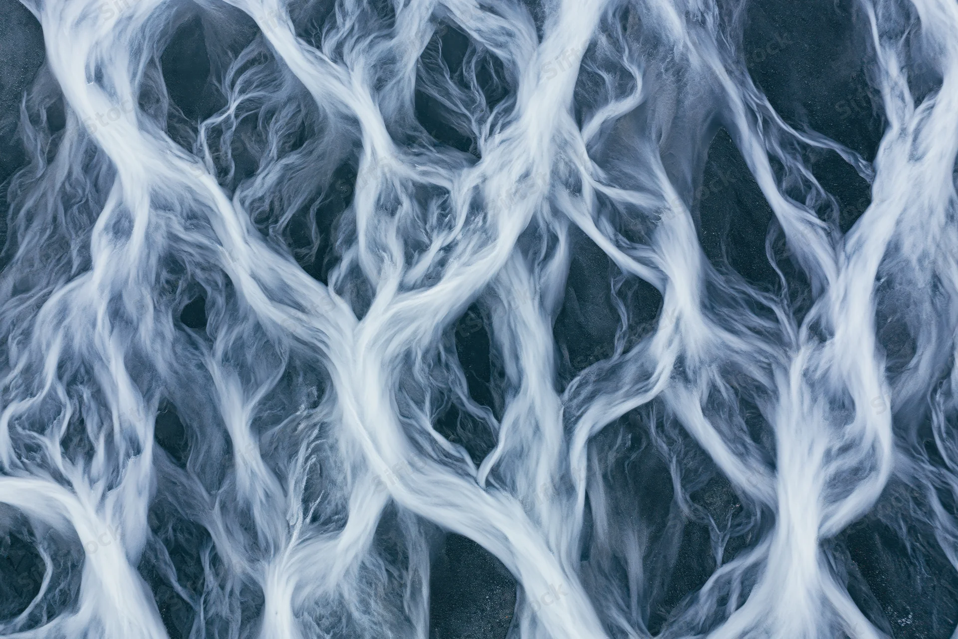 Aerial topdown view of a braided glacial river delta flowing across icy terrain