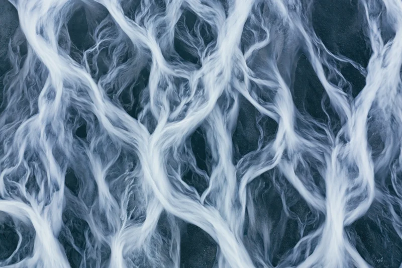 Aerial topdown view of a braided glacial river delta flowing across icy terrain