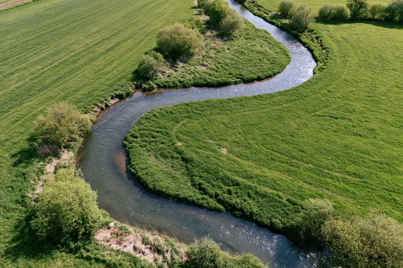 Aerial view of a narrow meandering river flowing through green fields