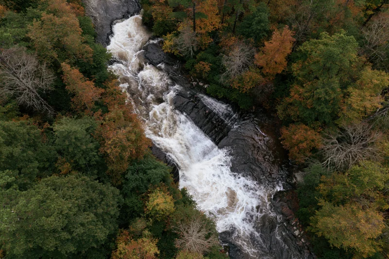 Aerial top-down view of a rushing waterfall cascading through a forested landscape in autumn