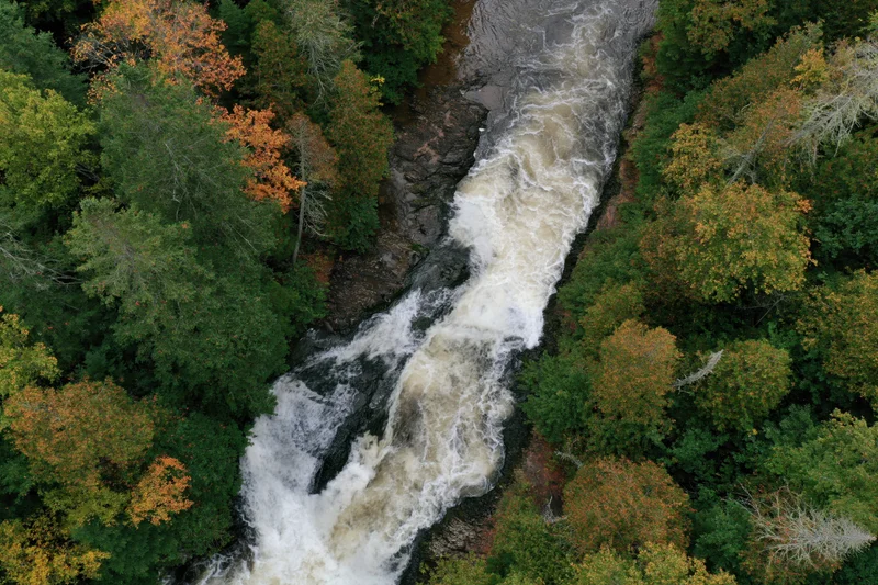 Aerial top-down view of a rushing waterfall cascading through a forested canyon in autumn