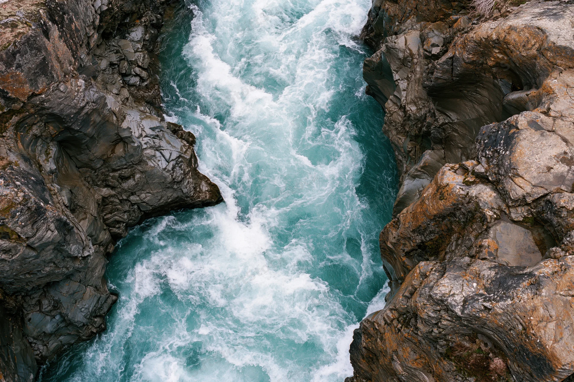 Turquoise river rushing through narrow rocky canyon from top-down aerial view