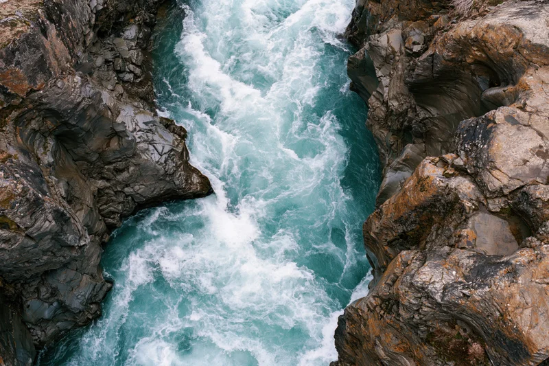 Turquoise river rushing through narrow rocky canyon from top-down aerial view