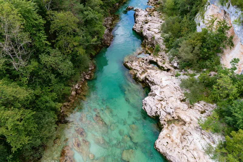 Aerial top-down view of a clear turquoise mountain river flowing through a rocky canyon surrounded by dense green forest