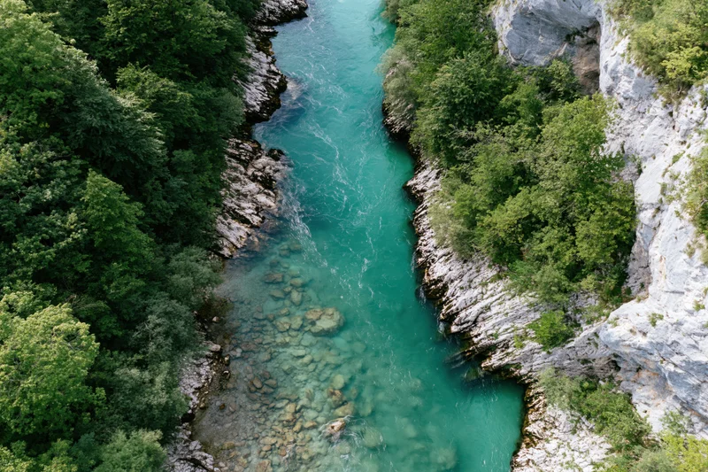 Aerial top-down view of a clear turquoise mountain river flowing through a rocky canyon surrounded by dense green forest