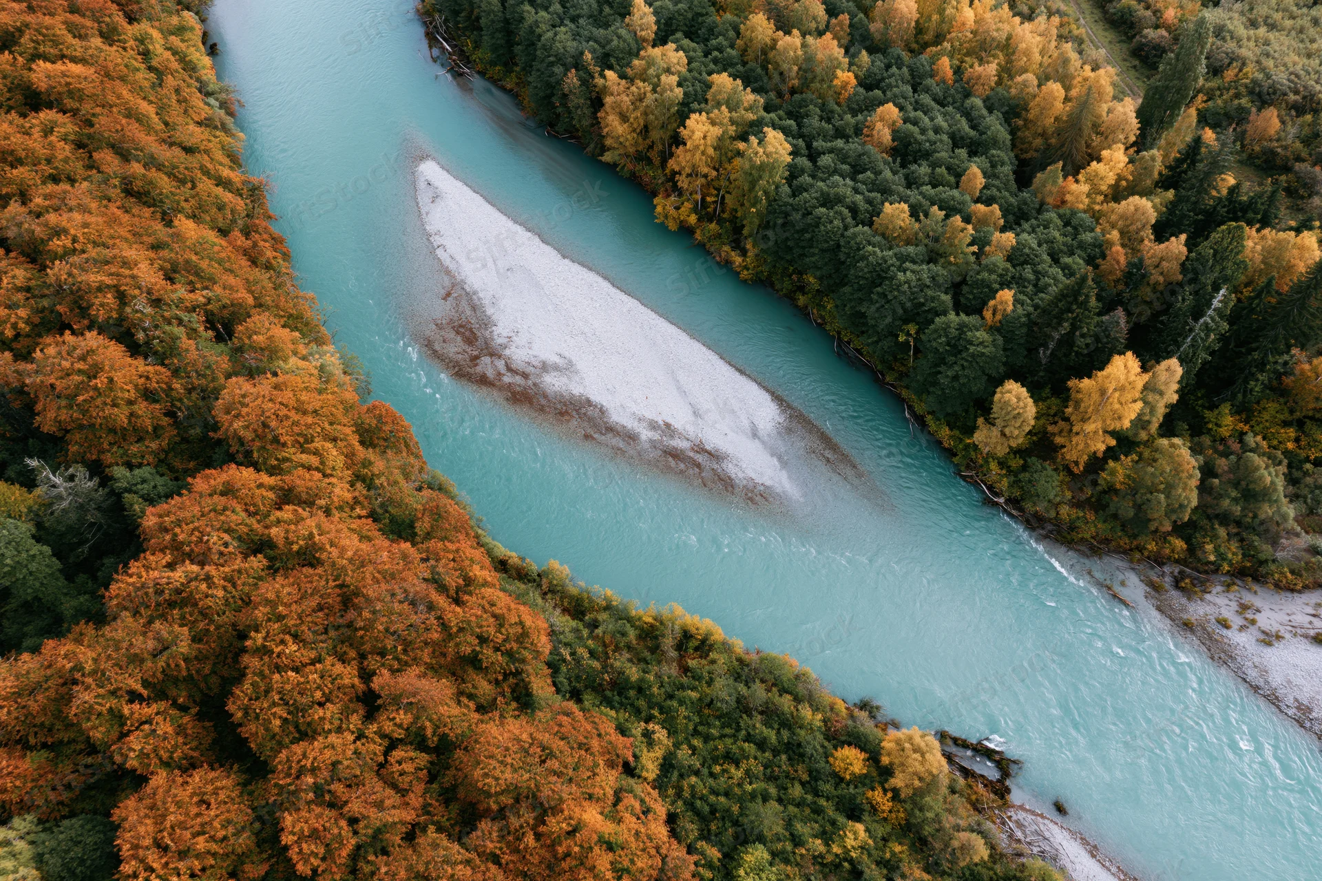 Aerial top-down view of a glacial turquoise river curving through autumn forest with orange and green foliage