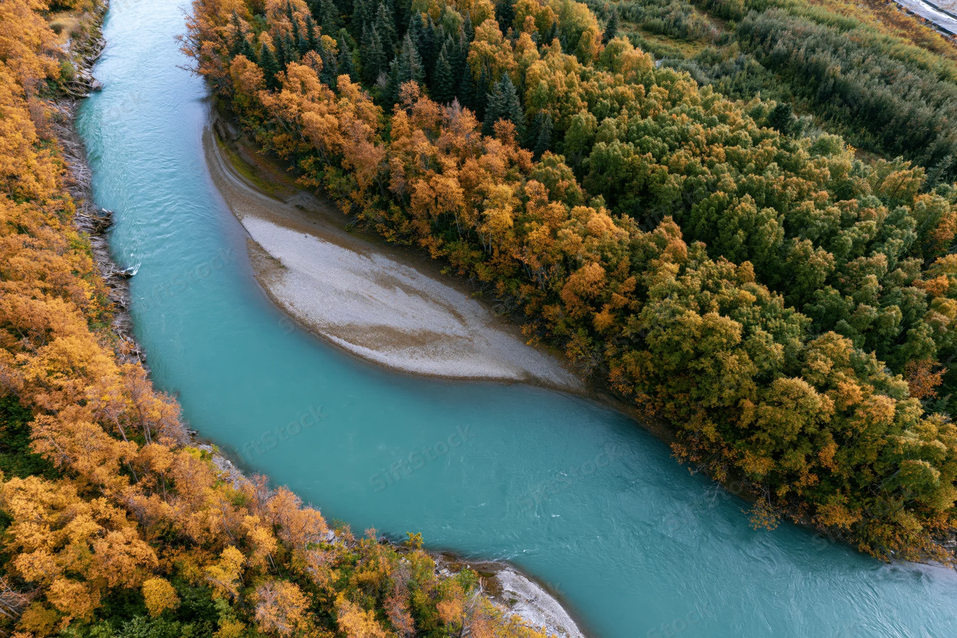 Aerial view of a turquoise river curving through autumn forest