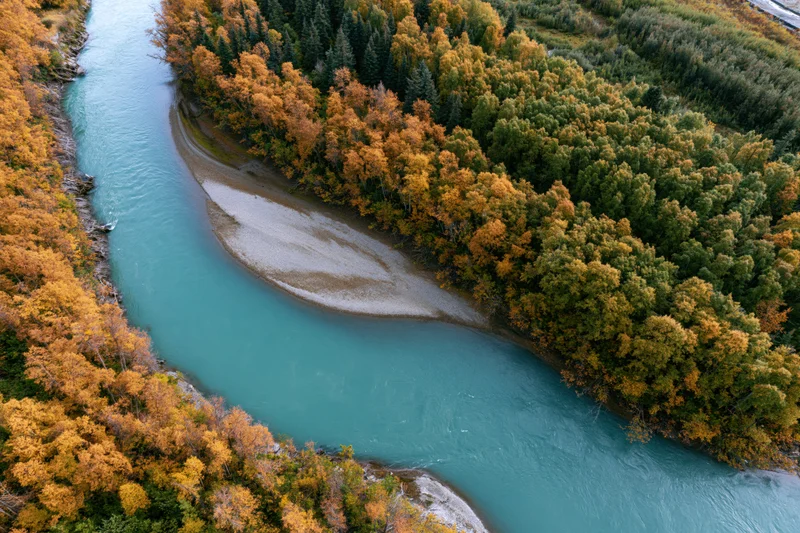Aerial view of a turquoise river curving through autumn forest