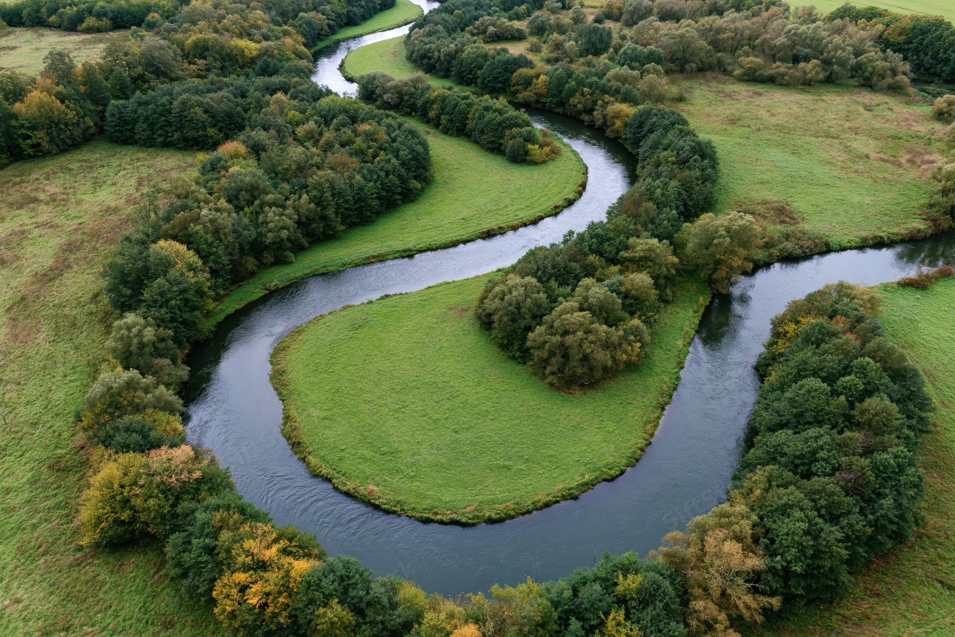 Aerial top-down view of a meandering river winding through green fields and forested areas