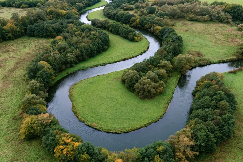 Aerial top-down view of a meandering river winding through green fields and forested areas