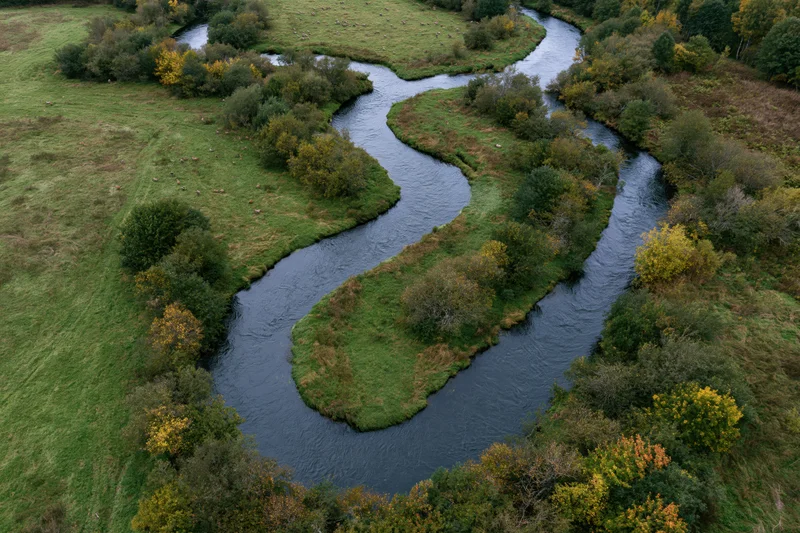 Aerial top-down view of a meandering river snaking through green fields and autumn trees