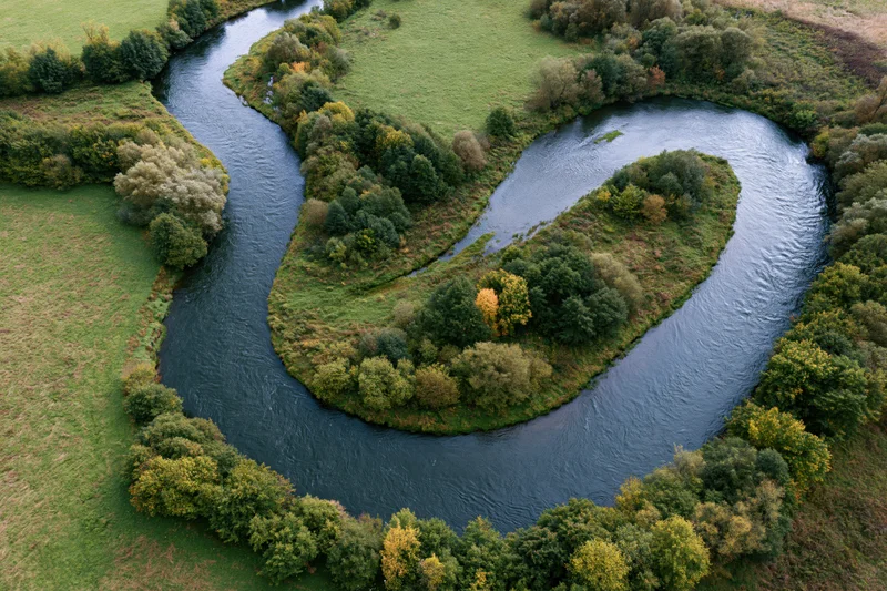 Aerial top-down view of a meandering river forming tight s-shaped bends through green forested countryside