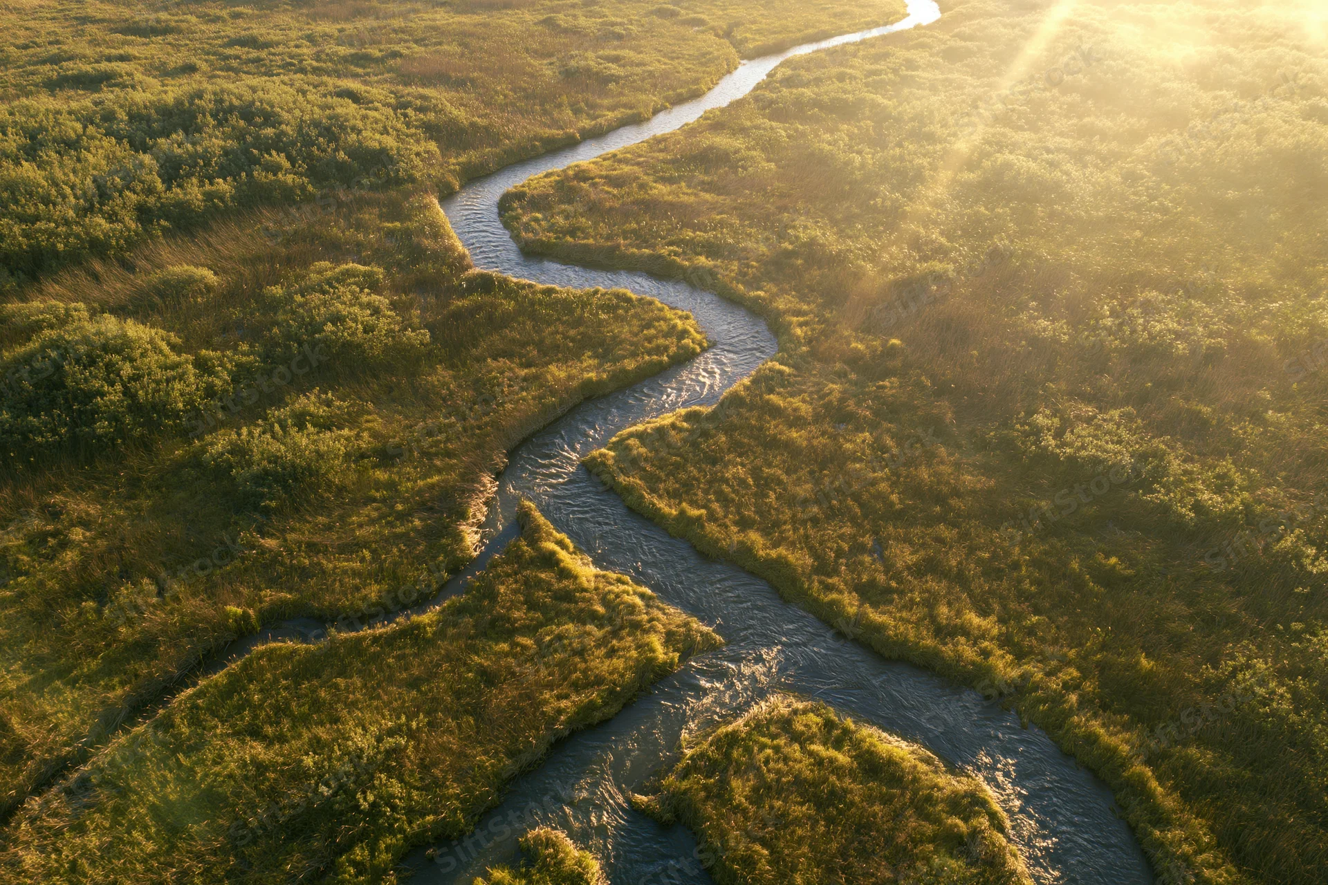 Aerial view of a winding river flowing through a marshy wetland at golden hour