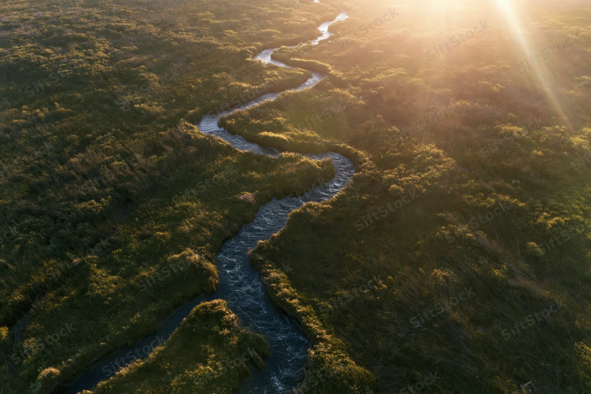 Aerial view of a winding river flowing through a marshy wetland at sunrise