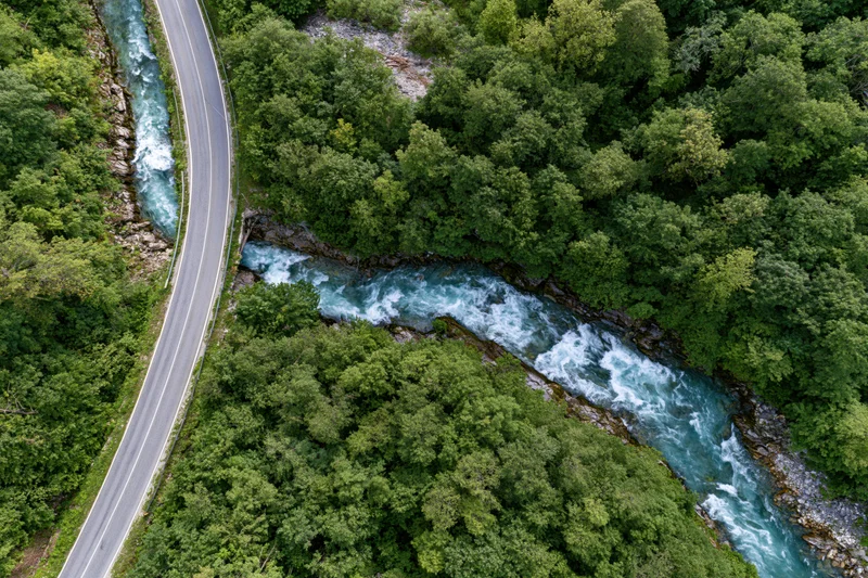Aerial top-down view of a winding asphalt road alongside a fast-flowing river through dense green forest