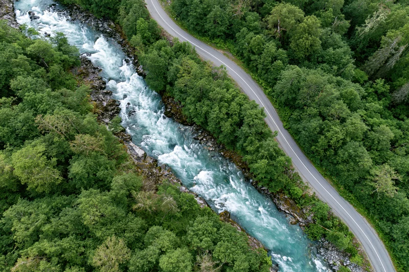 Aerial view of a winding road alongside a fast-flowing river through dense green forest