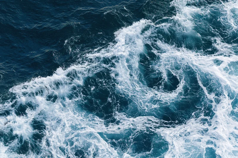 Aerial top-down view of deep ocean surface with churning white waves and foam