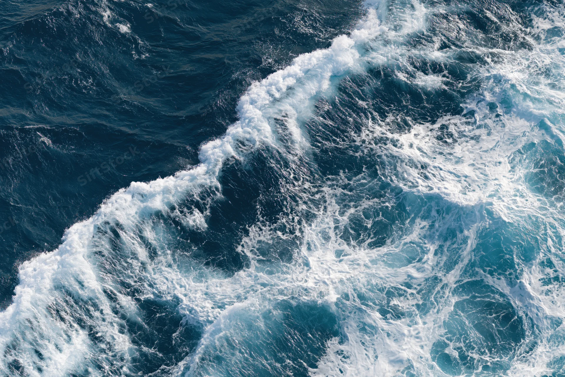 Aerial top-down view of churning ocean waves with white foam on deep blue surface