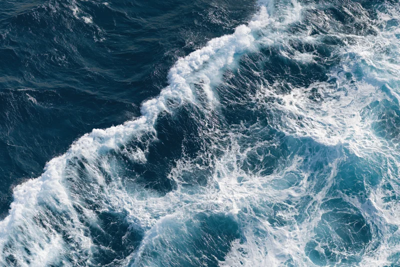 Aerial top-down view of churning ocean waves with white foam on deep blue surface