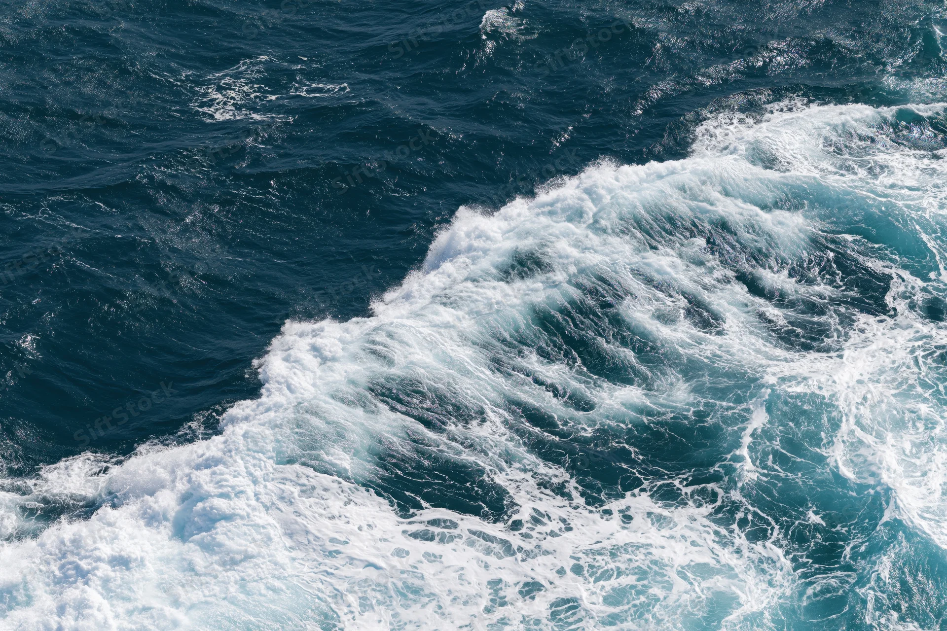 Aerial top-down view of churning ocean waves with white foam on deep blue surface