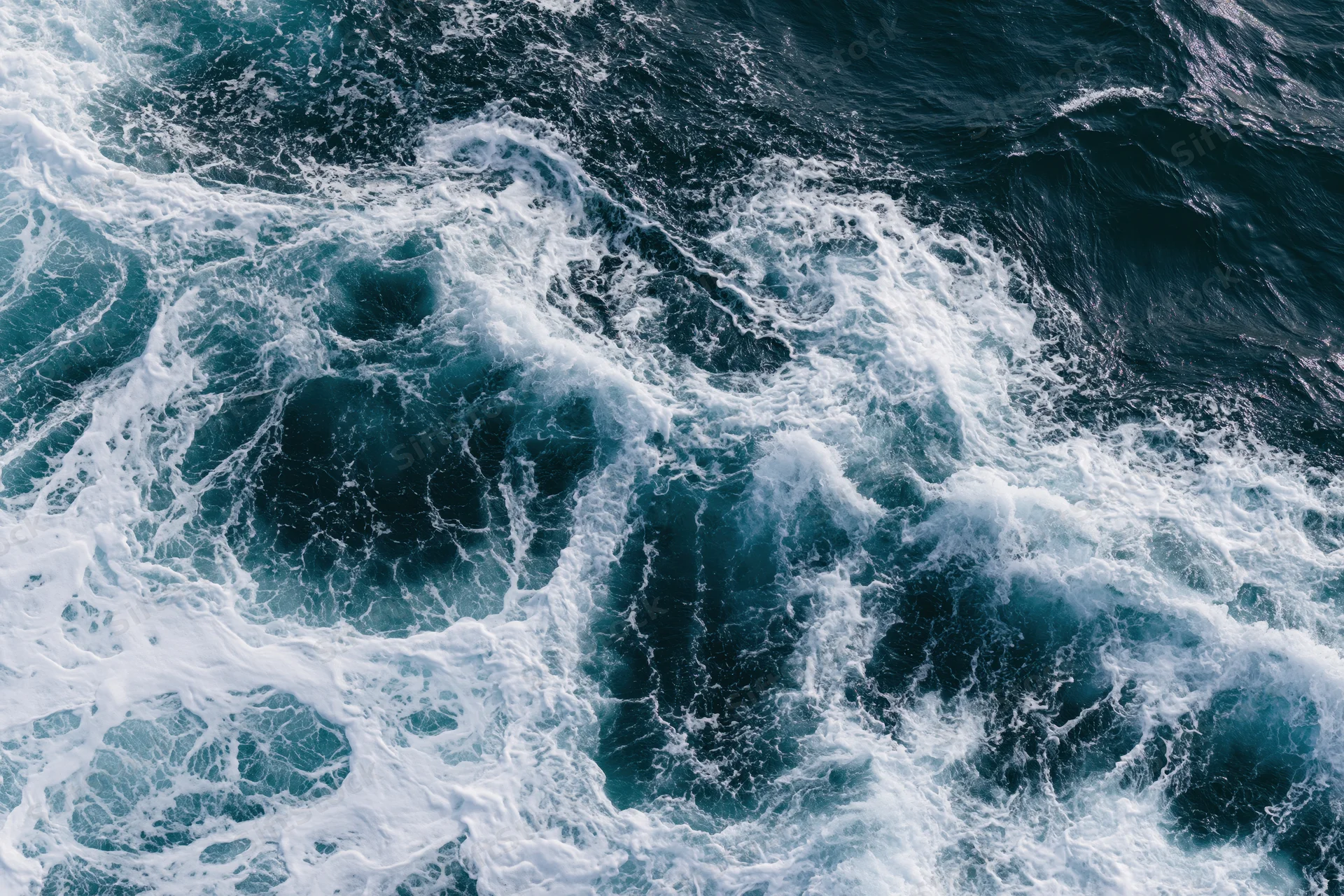 Aerial top-down view of churning ocean waves with white foam on deep blue surface