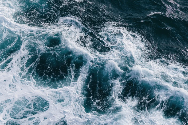 Aerial top-down view of churning ocean waves with white foam on deep blue surface