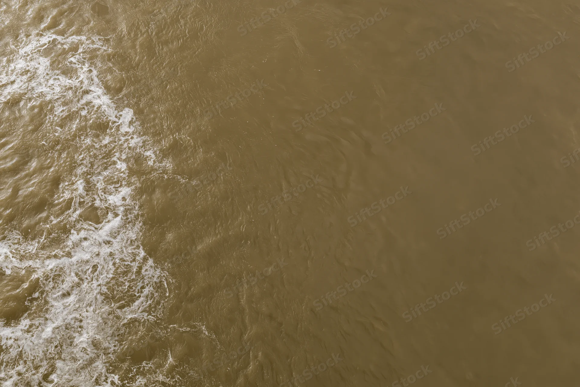Aerial top-down view of turbulent brown floodwater surface with white foam and ripples