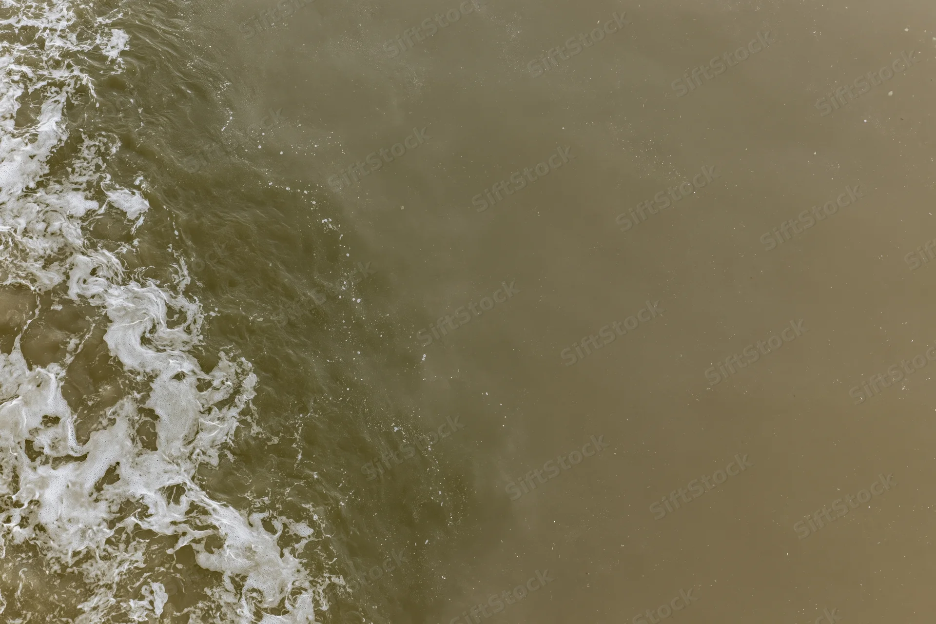 Aerial top-down view of turbid brown floodwater surface with white foam and ripples