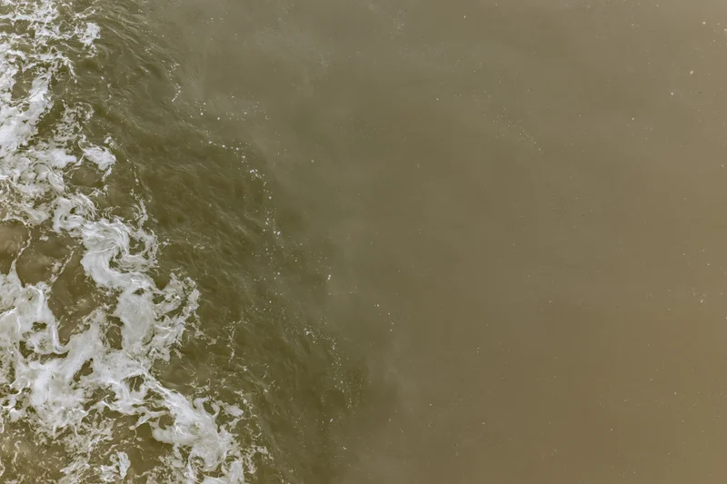 Aerial top-down view of turbid brown floodwater surface with white foam and ripples