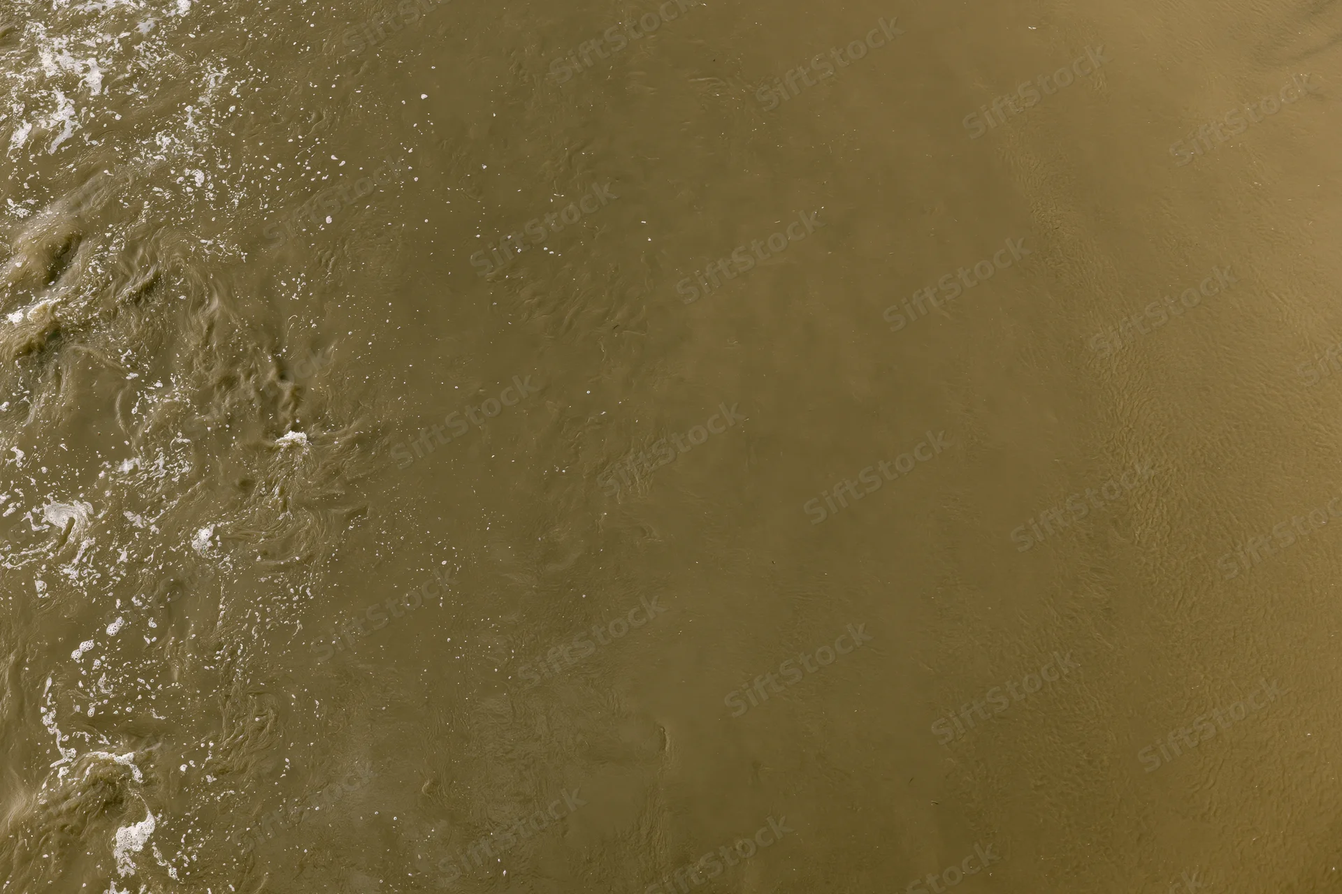Aerial top-down view of turbid brown floodwater surface with ripples and foam