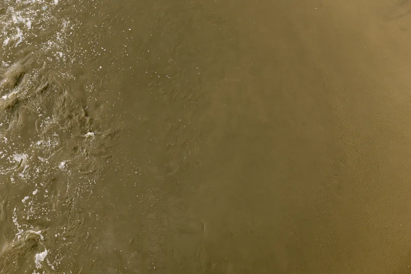 Aerial top-down view of turbid brown floodwater surface with ripples and foam
