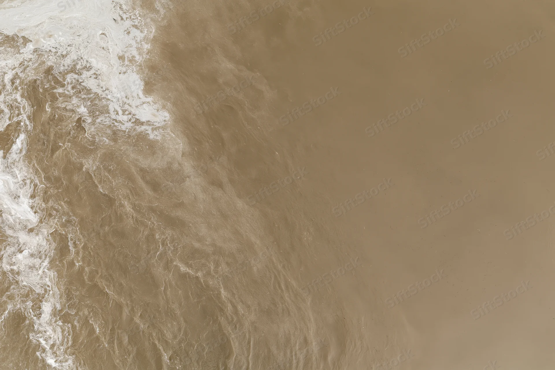 Aerial top-down view of turbid brown floodwater surface with foam and ripples