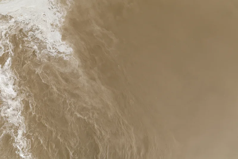 Aerial top-down view of turbid brown floodwater surface with foam and ripples