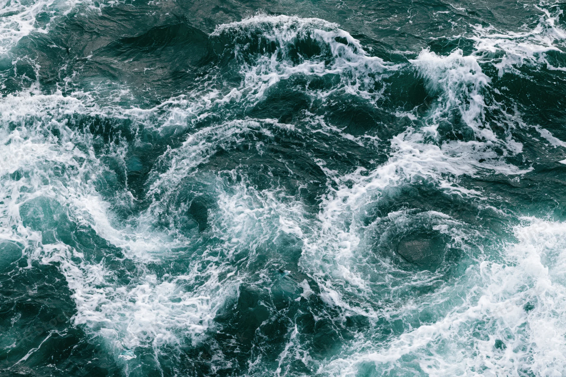 Turbulent ocean water with swirling waves and white foam from top-down view