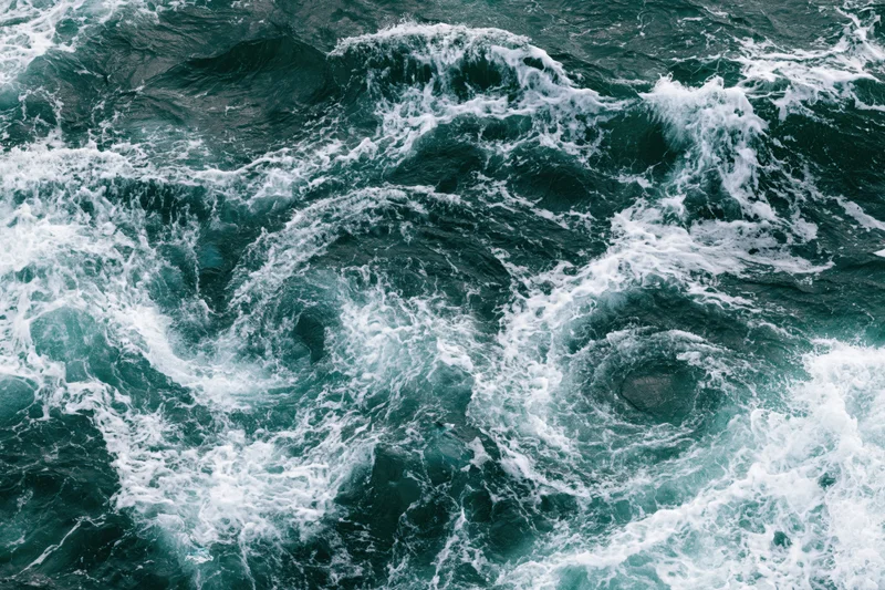 Turbulent ocean water with swirling waves and white foam from top-down view