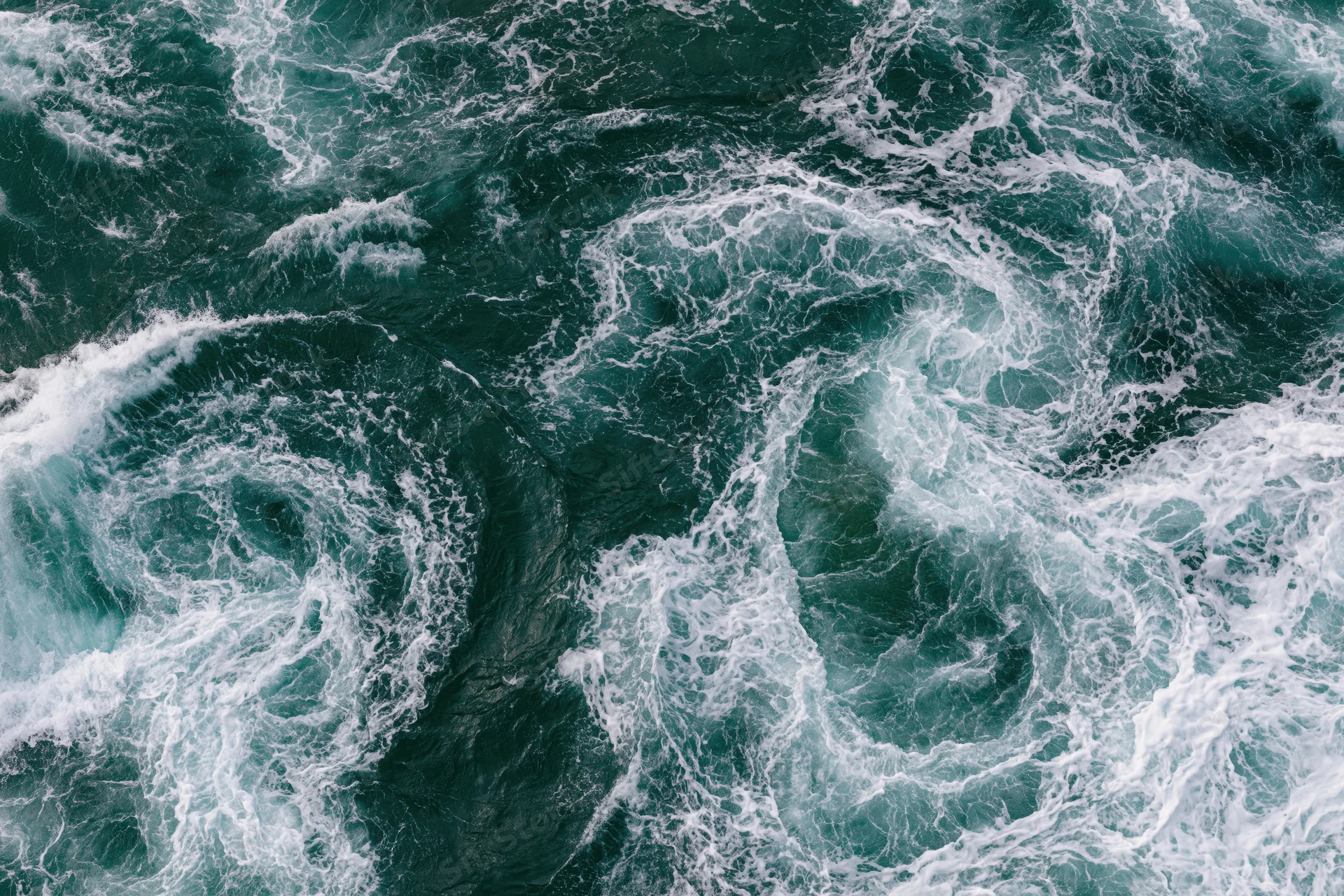 Aerial top-down view of turbulent ocean water with swirling foam and vortices