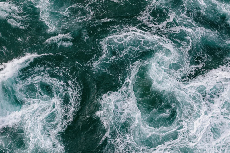 Aerial top-down view of turbulent ocean water with swirling foam and vortices