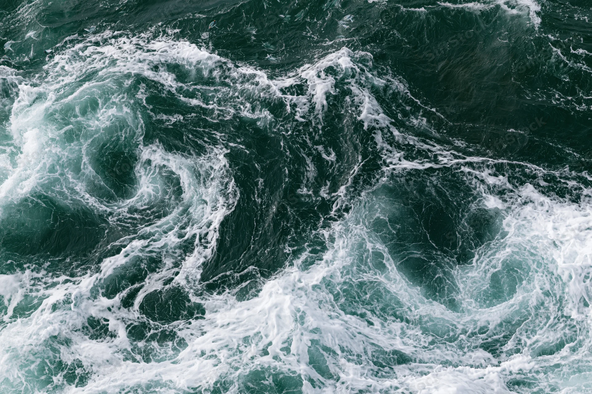 Turbulent ocean waves swirling with white foam from an aerial top-down view