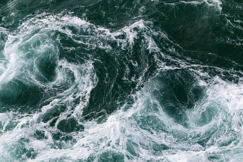 Turbulent ocean waves swirling with white foam from an aerial top-down view