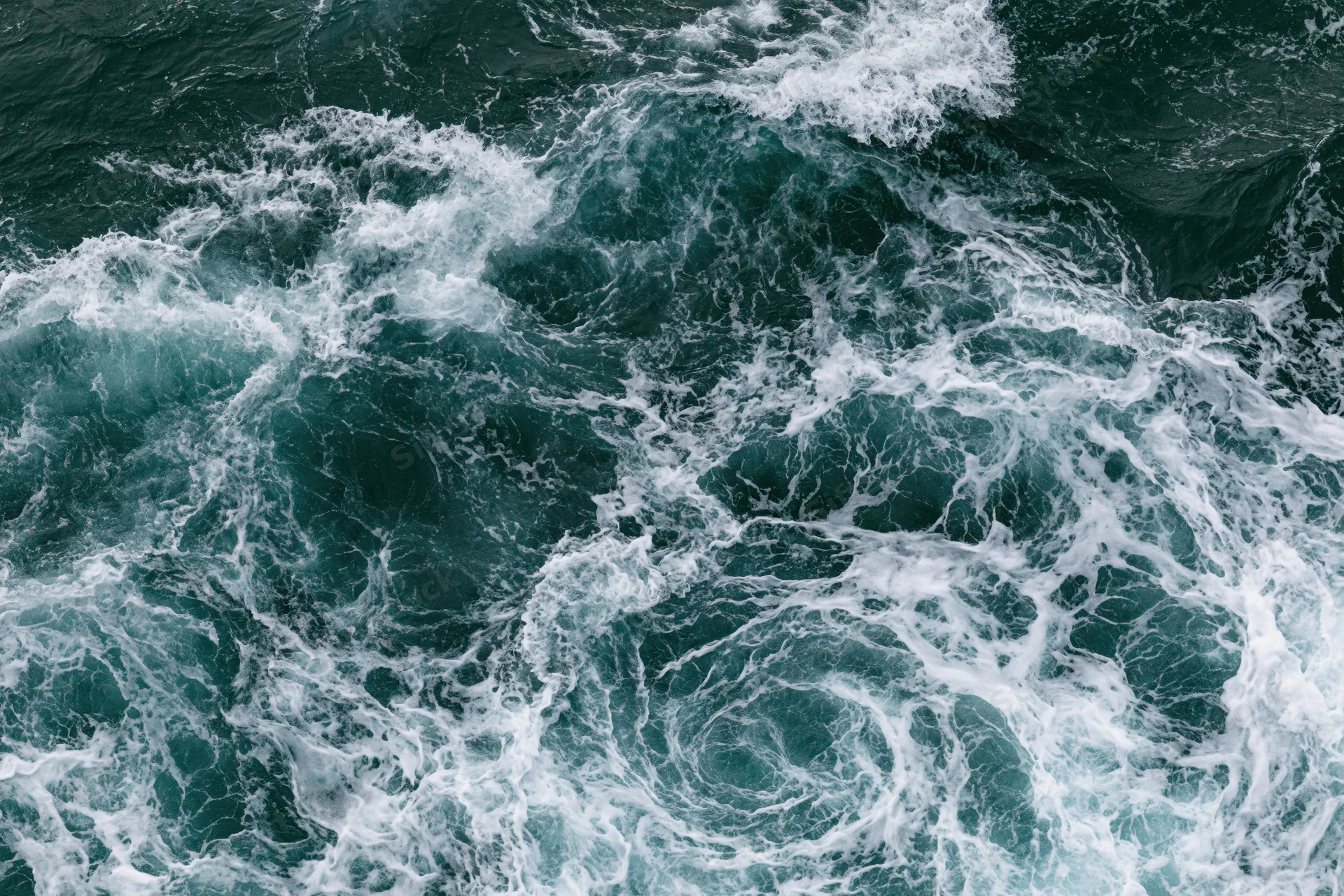 Top-down view of turbulent ocean waves swirling with white foam on the surface