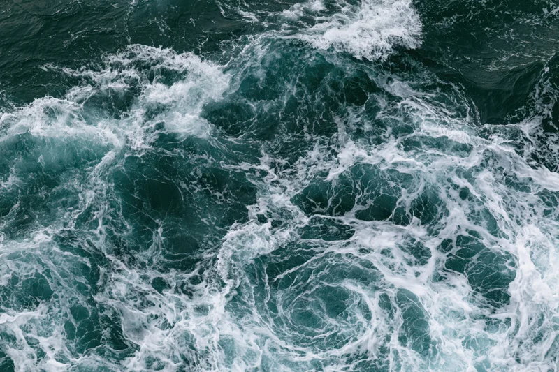 Top-down view of turbulent ocean waves swirling with white foam on the surface