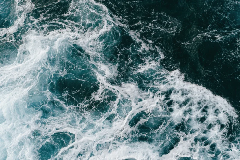 Aerial top-down view of turbulent ocean waves with churning white foam and deep blue water