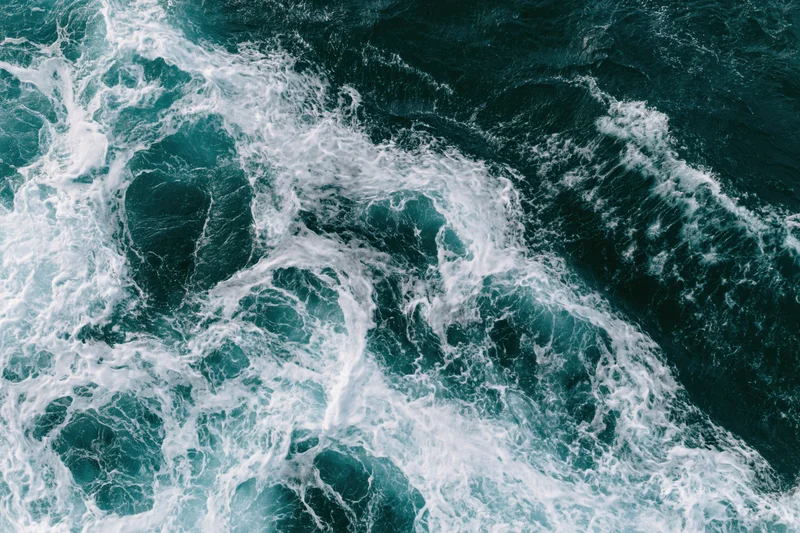 Aerial top-down view of turbulent ocean waves with churning white foam and dark blue water