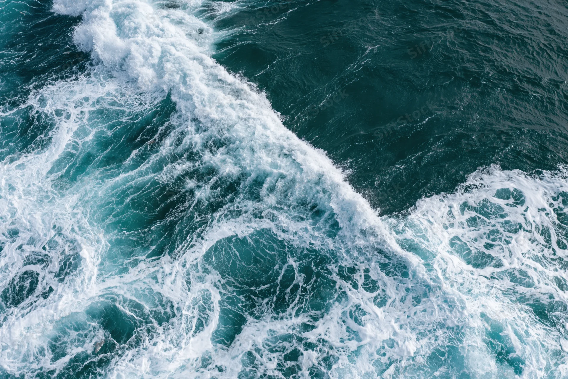 Aerial top-down view of turbulent ocean waves with churning white foam and deep blue water