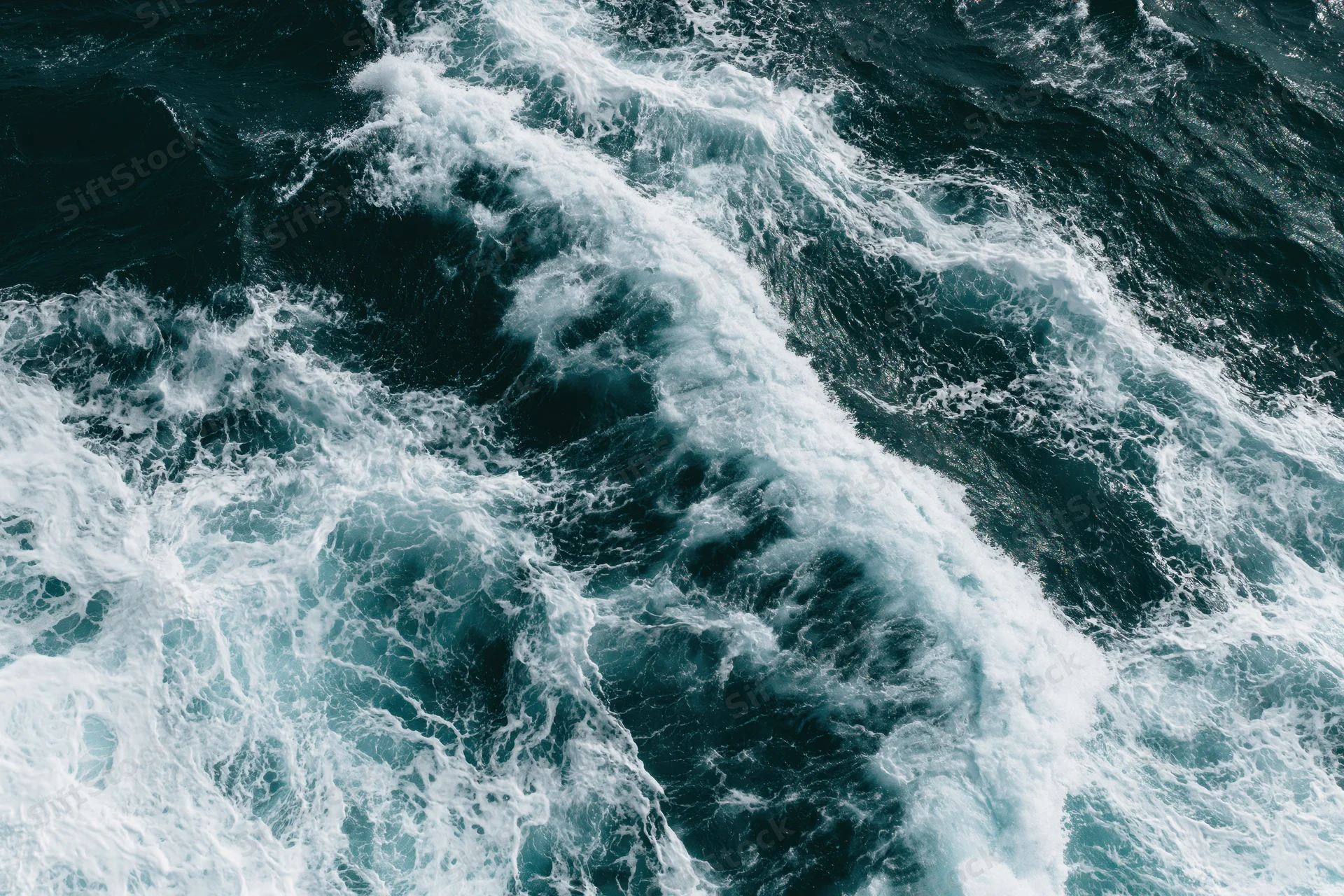 Aerial top-down view of turbulent ocean waves with churning white foam and dark blue water