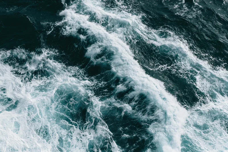 Aerial top-down view of turbulent ocean waves with churning white foam and dark blue water